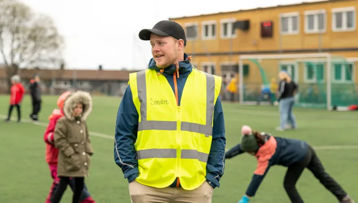 Kontaktlærer Sondre Brekke Valmork i utendørs arbeidsmiljø. I bakgrunnen ser vi noen barn.