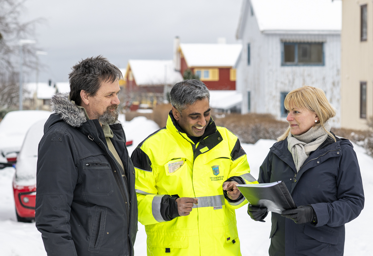 Prosjektleder Gnanavalluvan Vettivel i arbeidst&oslash;y i samtale med et par. I bakgrunnen skimtes flere hus.