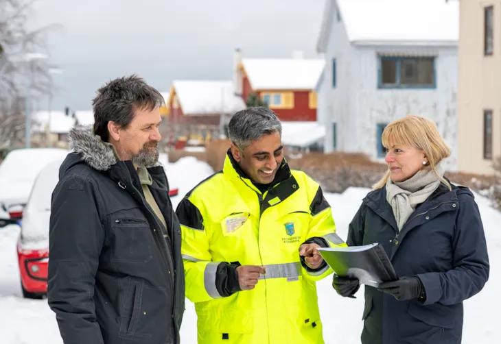 Prosjektleder Gnanavalluvan Vettivel i arbeidstøy i samtale med et par. I bakgrunnen skimtes flere hus.
