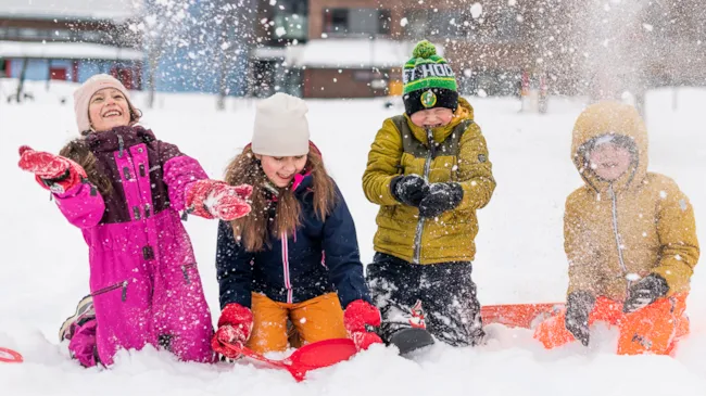 Fire barneskoleelever som leker seg ute i snøen.