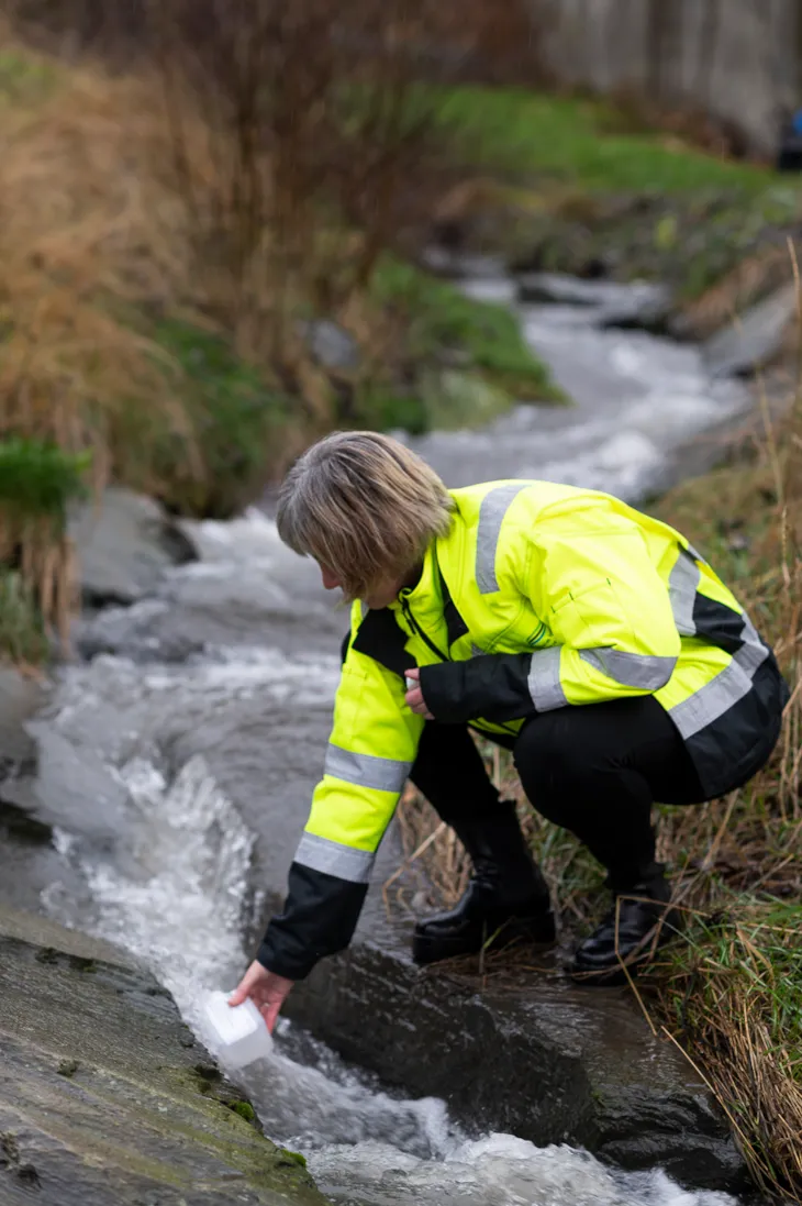 Cecilie sitter på huk ved en elv og tar en vannprøve.