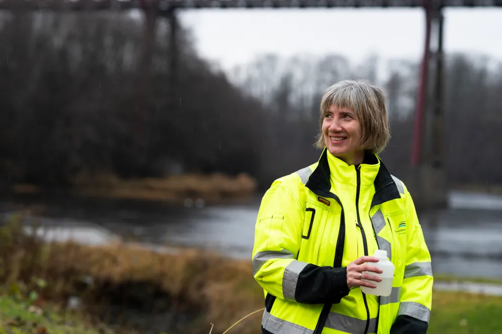 Cecilie portrettert ved en elv og en bro, med en vannprøve i hånda
