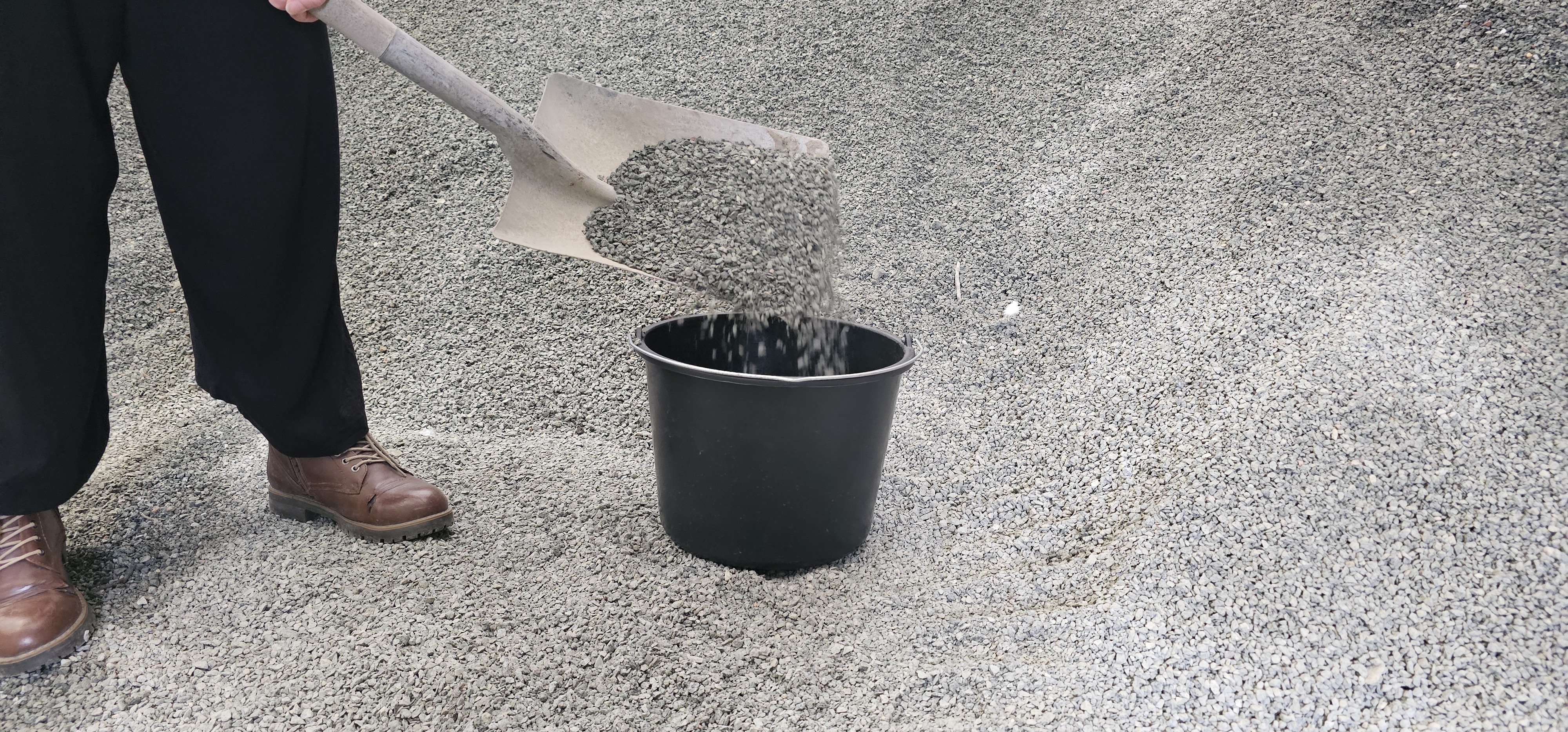 Bøtte som står i en sandhaug med en spade i hendene til den person