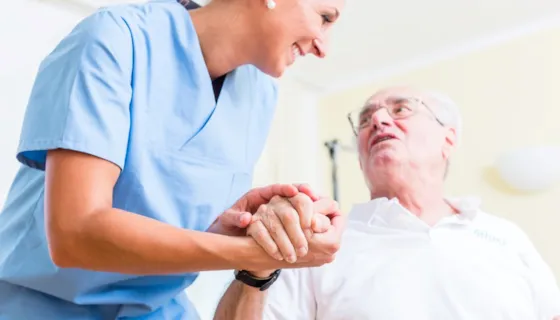 Sykepleier holder eldre mann i hånda