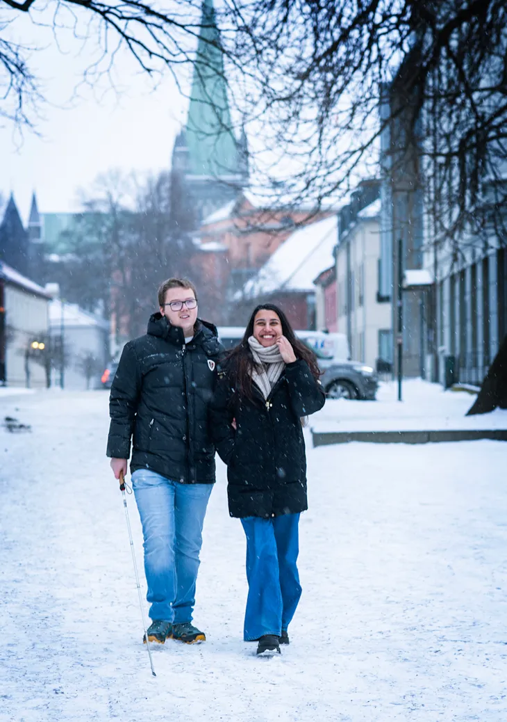 Mann med blindestokk sammen med funksjonsassistent.