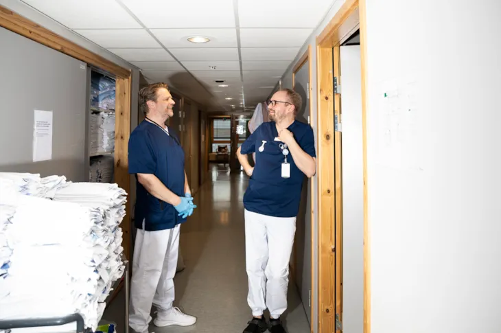 Helsefagarbeider Lars Erik slår av en lystig prat med en kollega i gangen