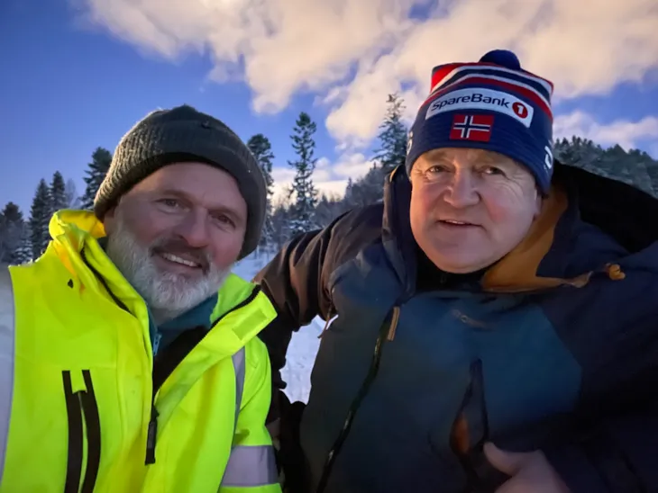 Et portrett av to menn som smiler mot kamera. De er ute og kledd for vintervær.