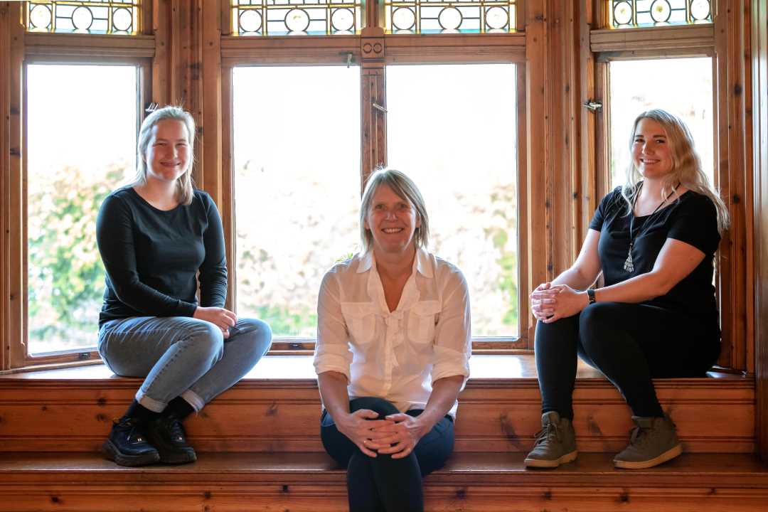 Tre damer sitter i en vinduskarm og smiler.