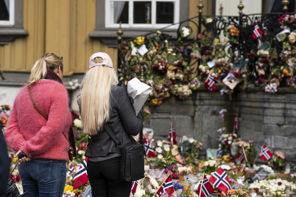 To damer står med ryggen til og ser på mange blomster foran Stiftsgården.