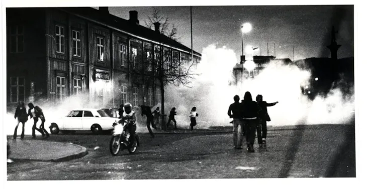 Bildet er fra slutten av 1970-tallet. Et svart-hvitt bilde viser Munkegata full av røyk. En person kjører forbi på moped. Det er mindre gjenger spredt i området.