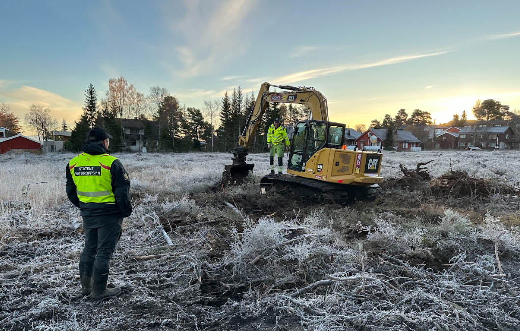 To men prater ut i naturen på Lianmyra ved siden av en traktor.