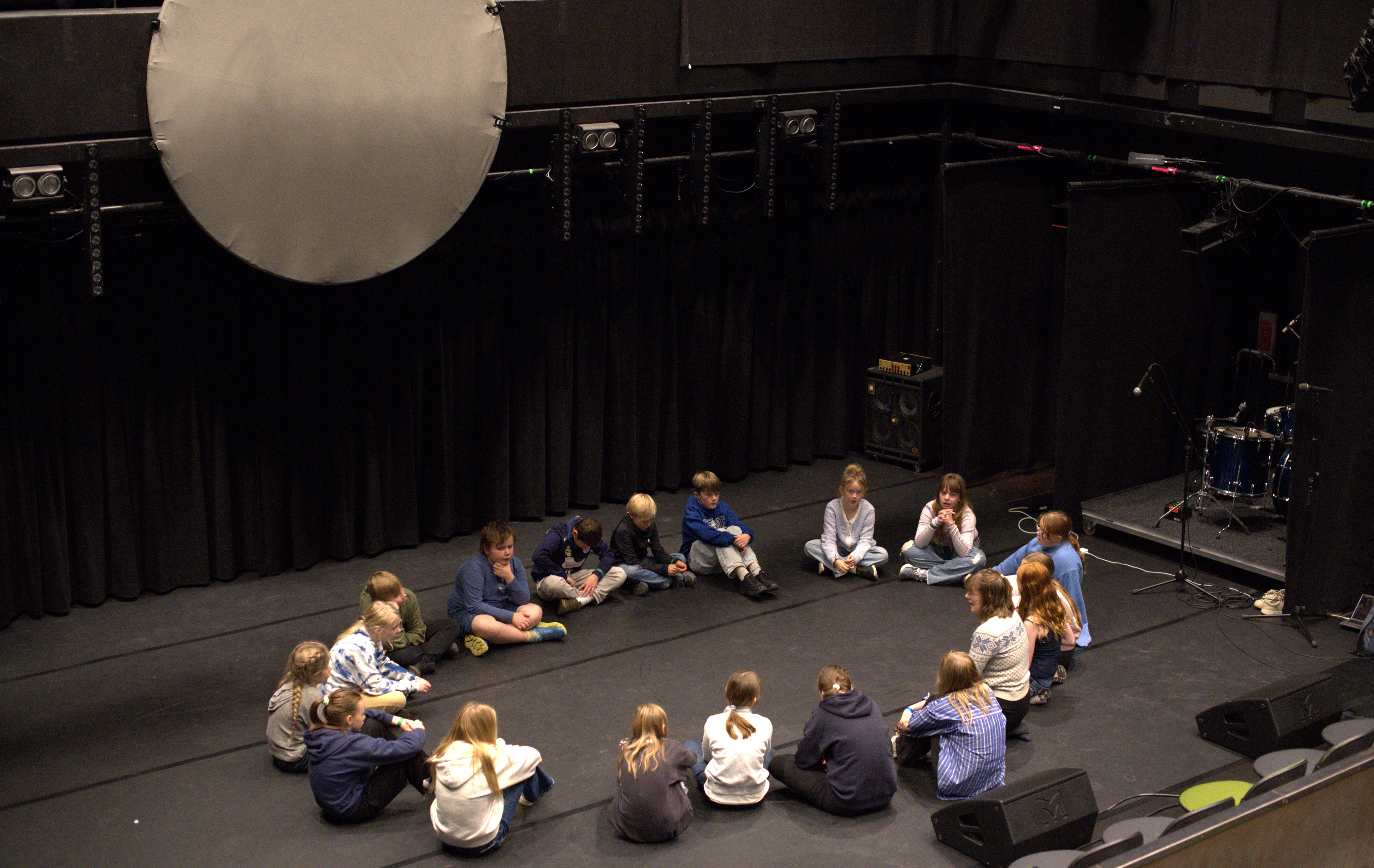 Elever undervises i joik og sitter i ring på scene.