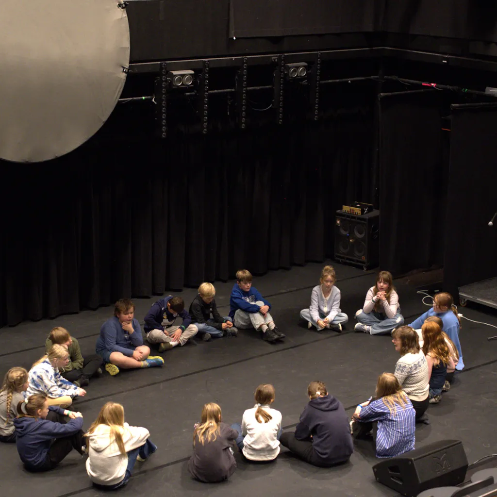 Elever undervises i joik og sitter i ring på scene.