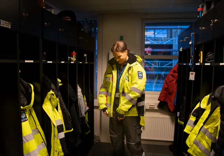 Foto av trafikkbetjent Marie i garderoben der hun kler seg om før dagens skift. Rundt henne er mange garderobeskap med uniformer.