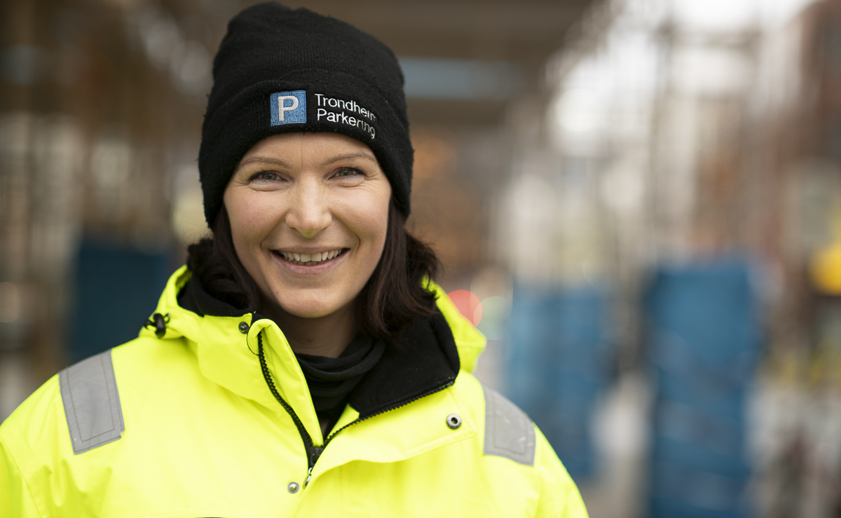 Foto av trafikkbetjent Marie i arbeidsuniform som smiler til kamera. Bakgrunnen er utydelig.