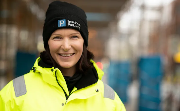 Foto av trafikkbetjent Marie i arbeidsuniform som smiler til kamera. Bakgrunnen er utydelig.