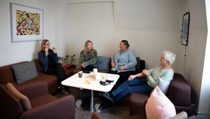 Fire kvinner sitt i ei sofagruppe og snakkar saman.