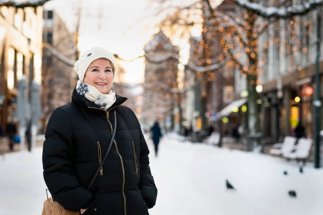 Portrett av Kirsti Vandbakk i Nordre om vinteren, med vinterbelysning og snø på gata i bakgrunnen.
