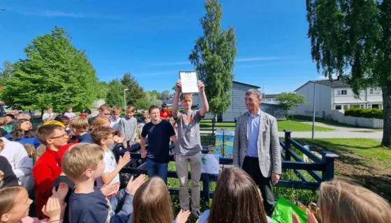 Elever ved Flatåsen skole mottar beviset på at skolen har fått Grønn Barnebys pris for 2022. Juryleder Geirmund Lykke overrakte prisen til elever på 10. trinn.