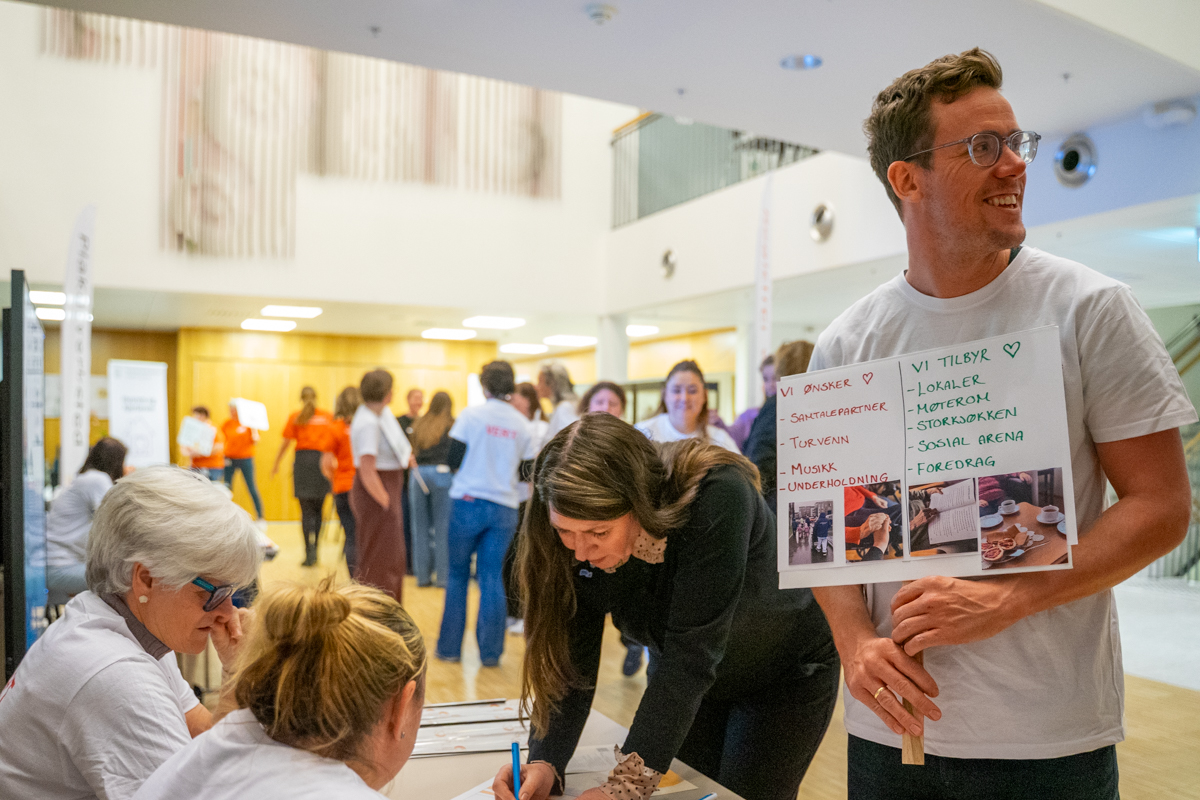 En mann og en kvinne signerer kontrakt og smiler. I bakgrunnen ser man mange folk i lokalet.