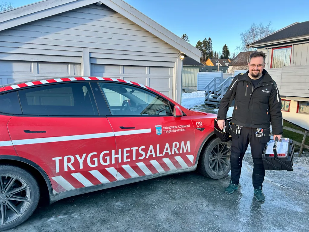 Tekniker i trygghetspatruljen står foran rød bil med verktøykoffert.