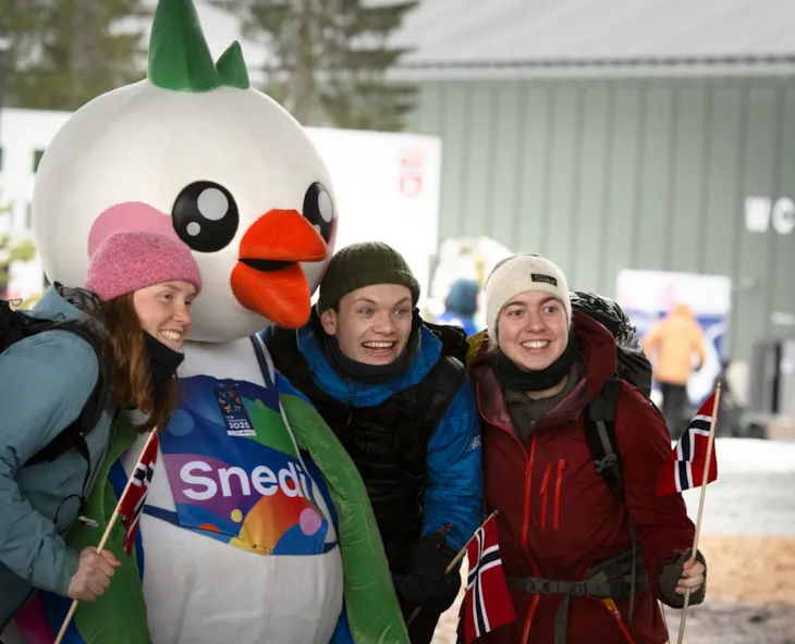 Tre unge voksne smiler mot kamera sammen med maskotten Snedig.