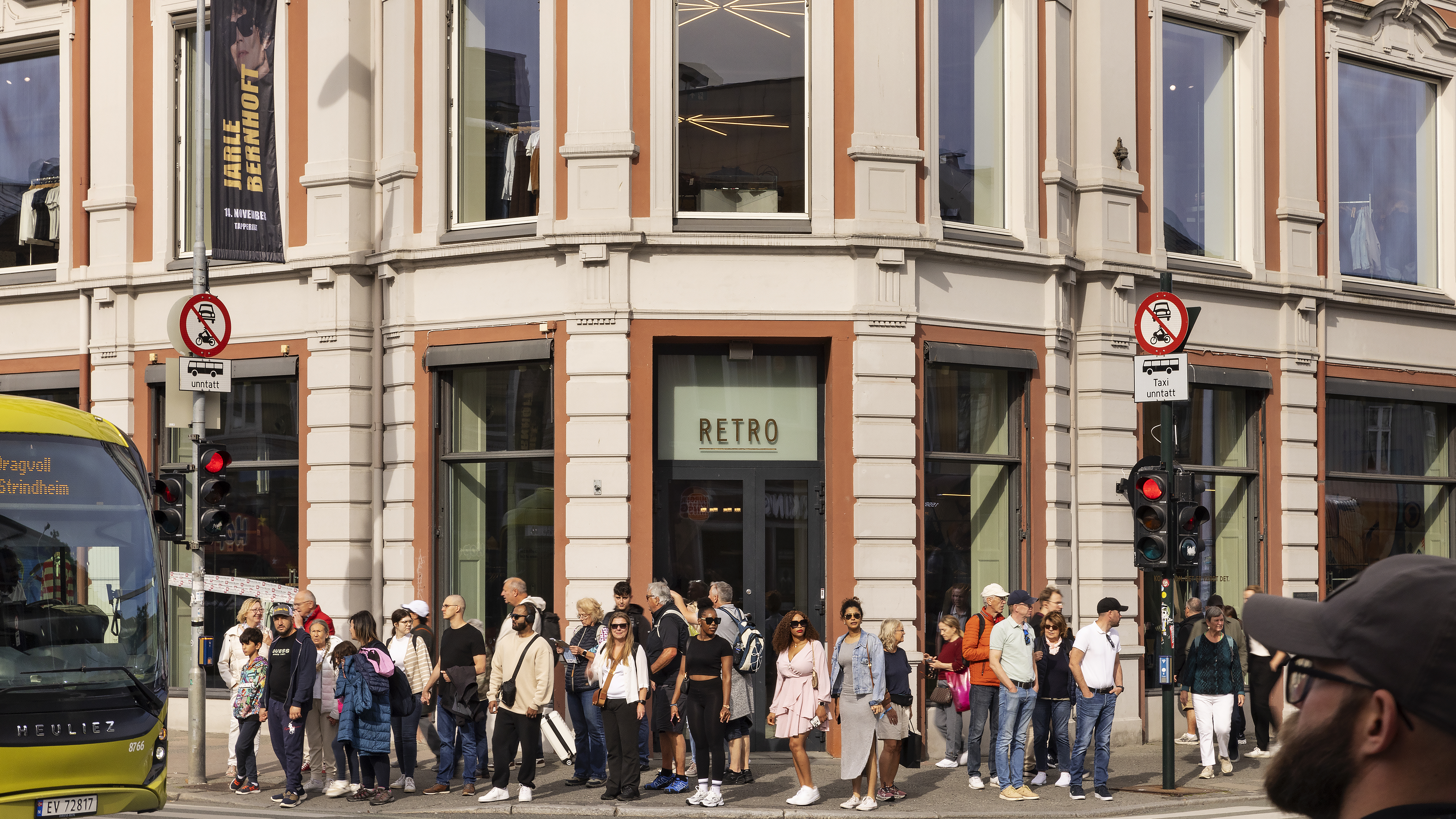 N&aelig;rbilde av bygningens hj&oslash;rne med mange mennesker foran som st&aring;r og venter p&aring; gr&oslash;nt lys ved fotgjengerovergang