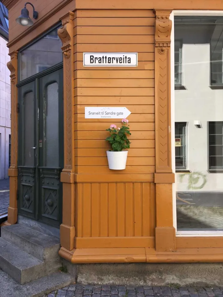 Hushjørne med snarveit-skilt og plante på vegg