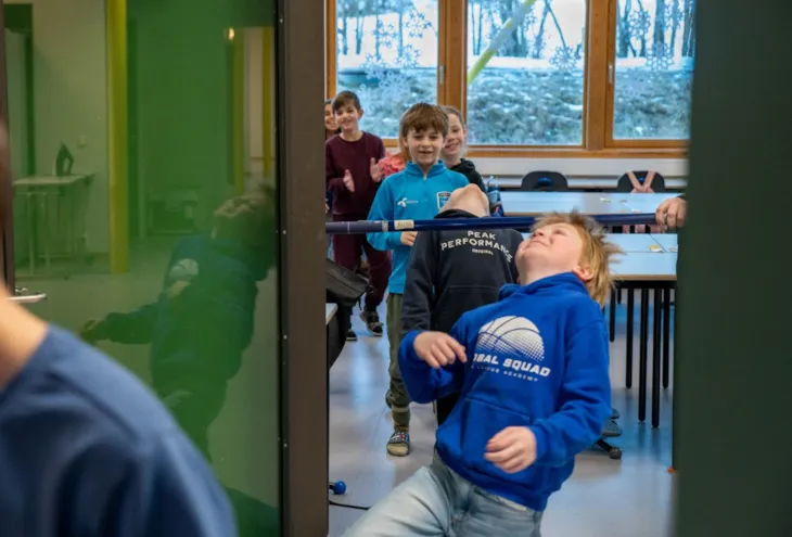 Ei gruppe med elever i 3. klasse er på veg ut av klasserommet, og dansar limbo under ei stang i døra.