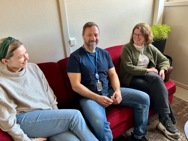 Representanter fra kommunens MO-senter sitter i en rød sofa sammen med en kvinne fra Steg for steg.