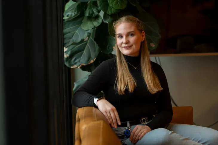 Emilie sitter i en brun skinnsofa og smiler til kamera.