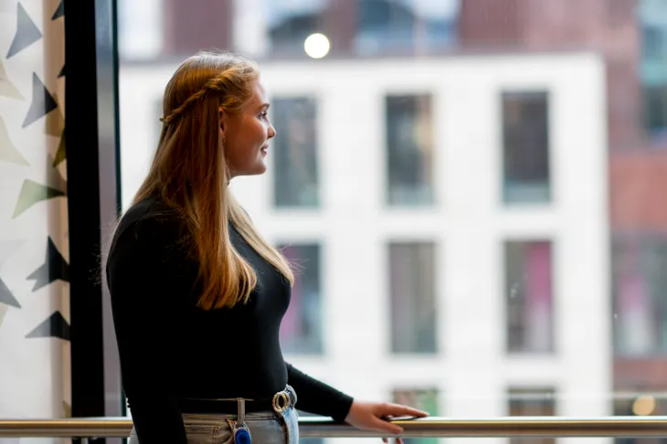 Emilie står ved et vindu inne på kontoret og ser ut.