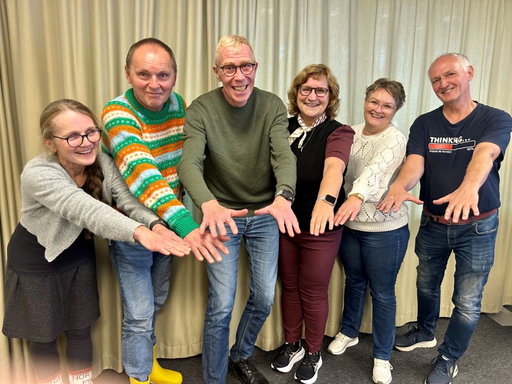 Seks 65-åringer på rekke som holder ut hendene sine.