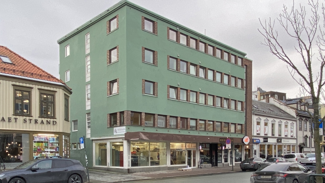 en gr&oslash;nn murbygning i fire etajer med enkle vinduer