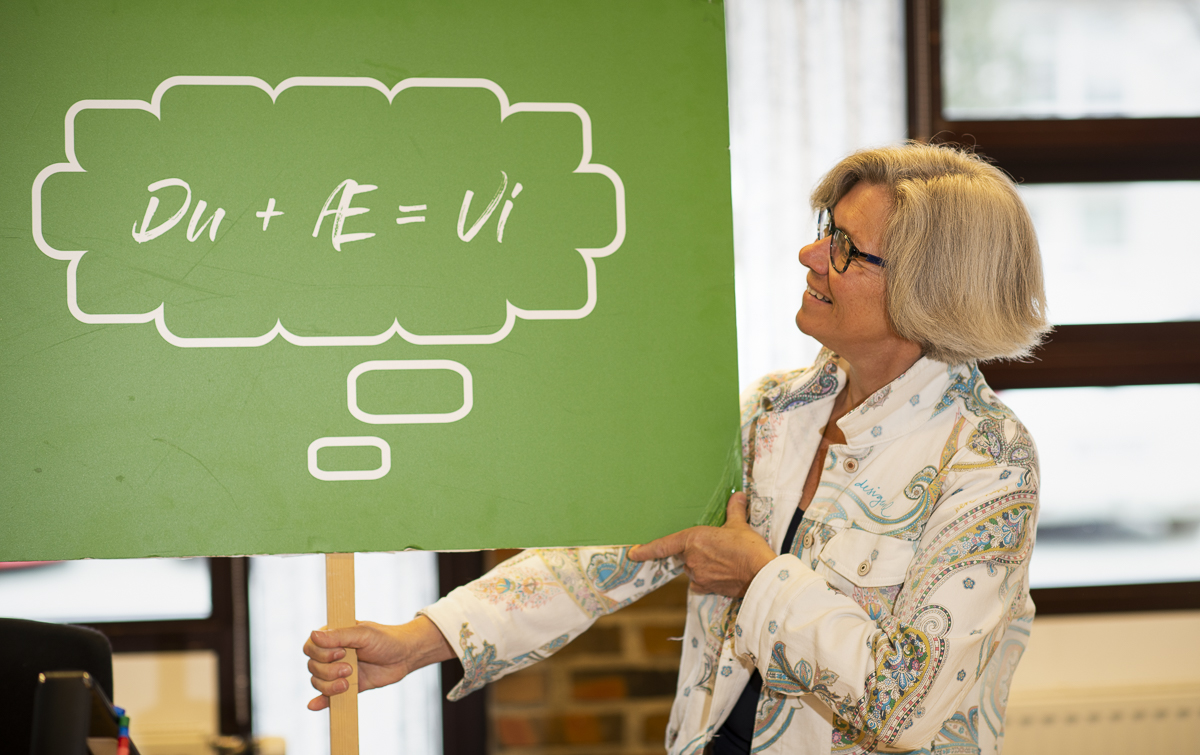 Rektor Gro Kristansen holder et skilt med p&aring;skriften "Du + &aelig; = vi" inne i et klasserom.