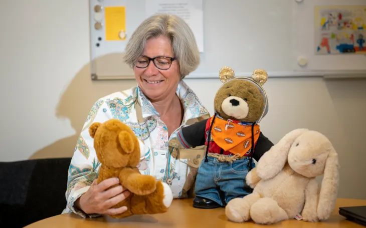 Rektor Gro Kristiansen ved Dalgård skole og ressurssenter sitter i en sofa med tre bamser i fanget.
