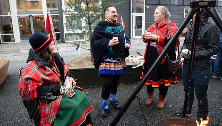 To kvinner og ein mann, alle kledd i kofter, pratar saman og er i godt humør.