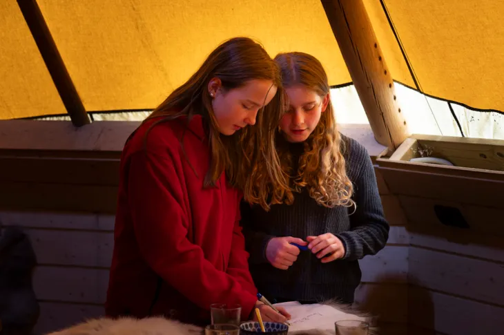 To elever skriver navn på sitteunderlag av reinskinn.