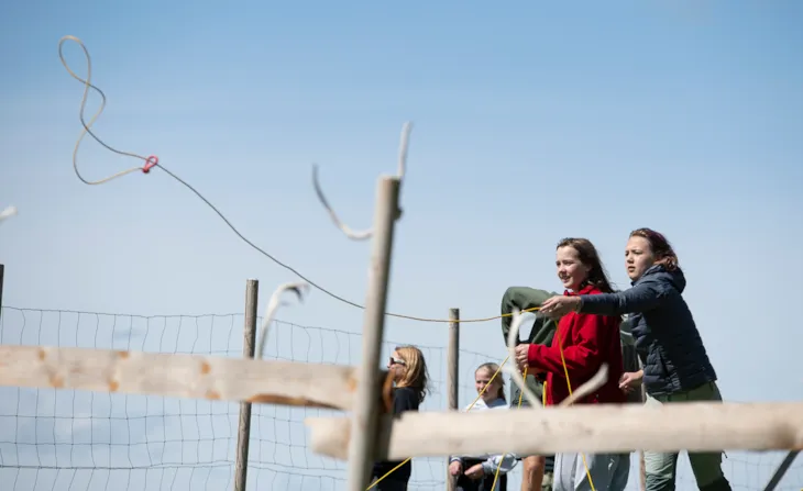 Elever som øver seg på å kaste lasso. Gjerde med reinshorn på i forkant i bildet.