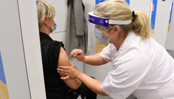 Sykepleier stikker vaksinesprøyte i arma på en kvinne.