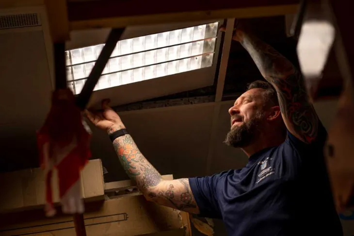 Driftsleder Kim Høglund Olsen står oppe i ei gardintrapp og skifter et lysrør i taket.