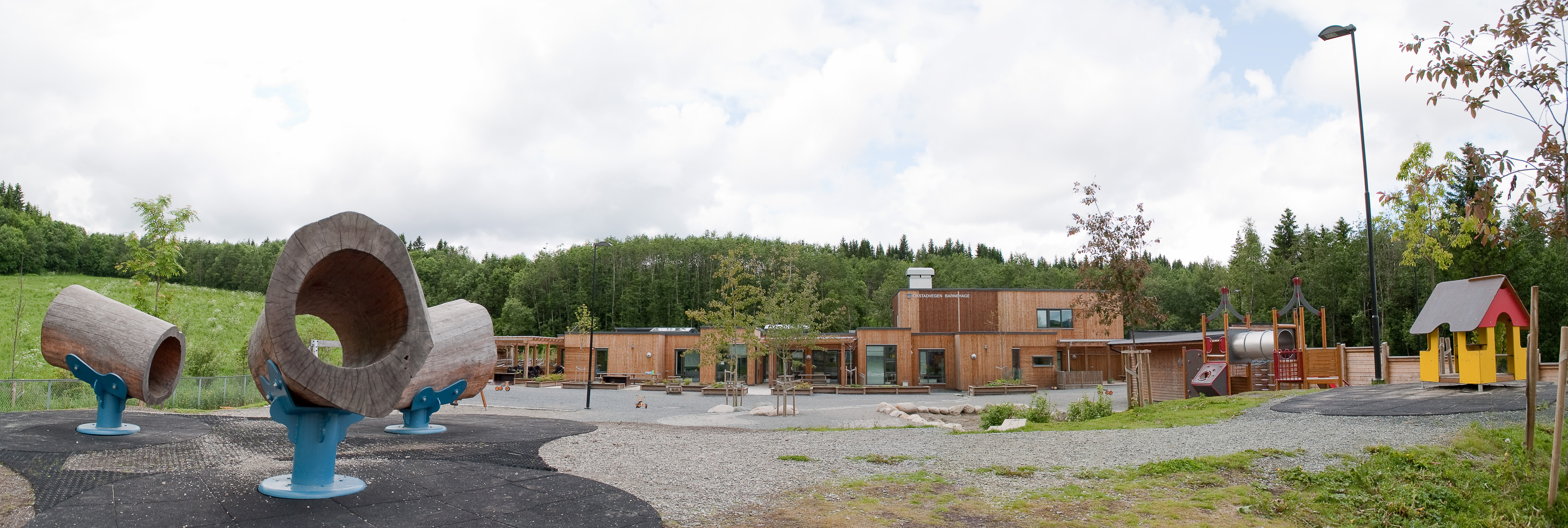 Lekeområde og Okstavegen barnehage sin trebygning i et grønt område