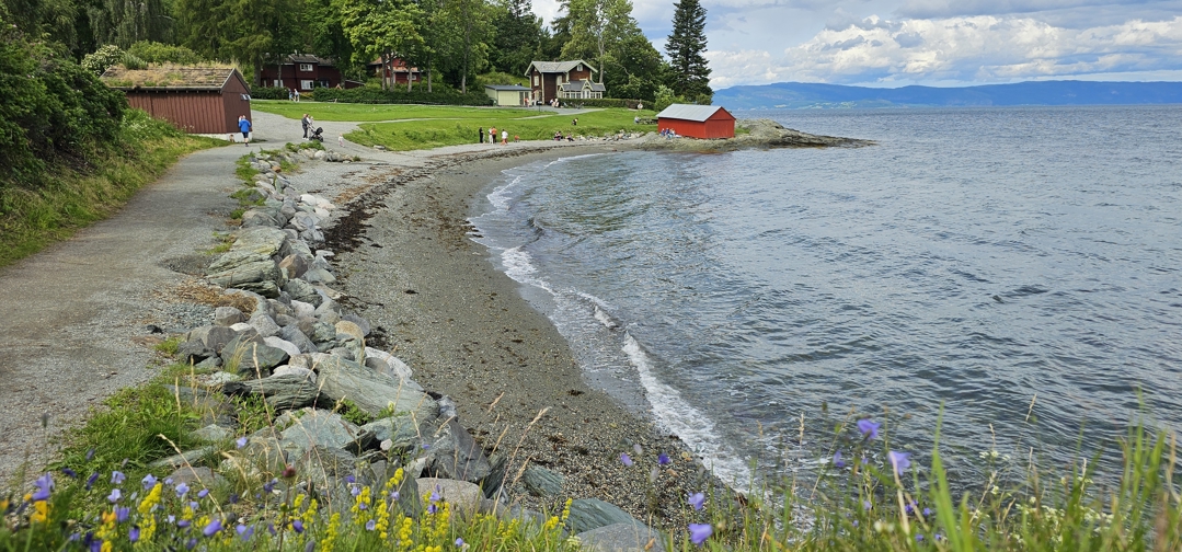 Foto av strand og sti med bygninger i bakgrunnen