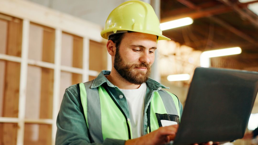 Mann med hjelm og refleksvest som jobber ved en pc