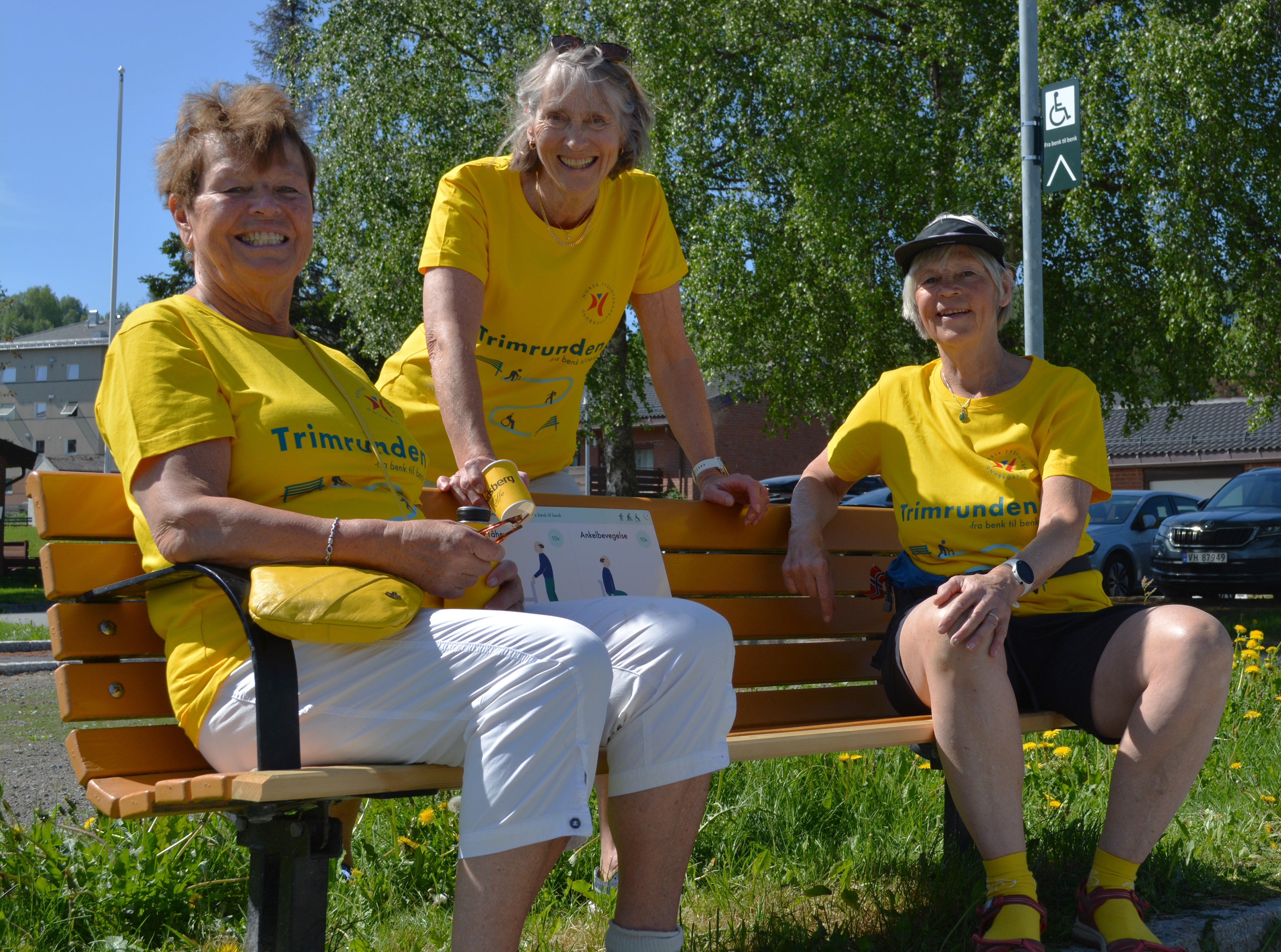 Tre ansatte med gule skjorter p&aring; en benk