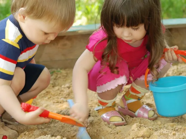 en gutt og en jente som bruker spade i sandkassa