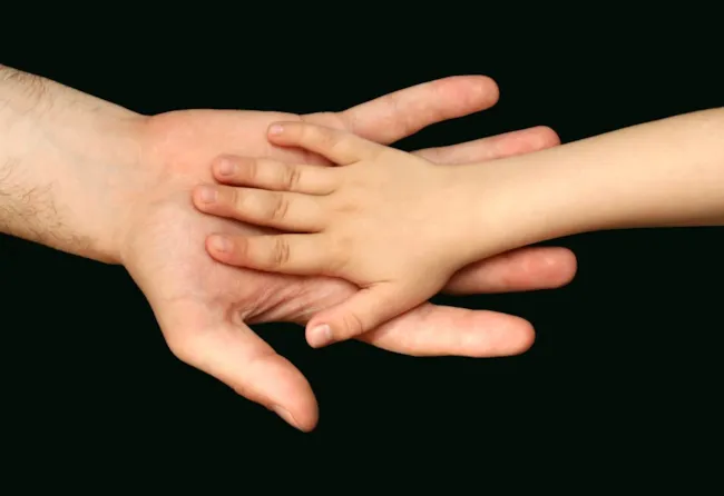 En voksenhånd og en barnehånd på svart bakgrunn