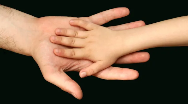 En voksenhånd og en barnehånd på svart bakgrunn