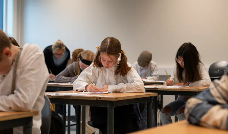Seks elever sitter ved pultene sine og konsentrerer seg om å skrive løkkeskrift.