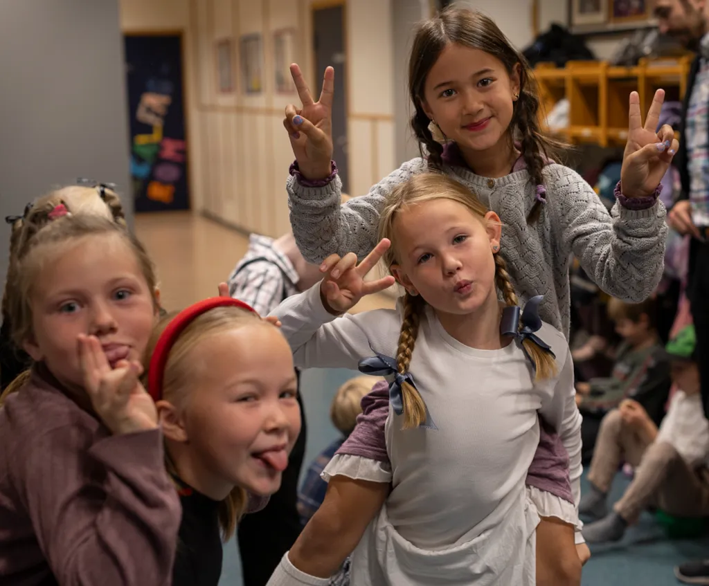 Fire jenter i 3. klasse tuller og smiler til kamera. De har flettet hår med sløyfer i og gammeldagse klær.